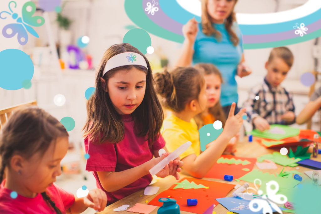 The group of children are sitting at a table and making an applique of colored paper